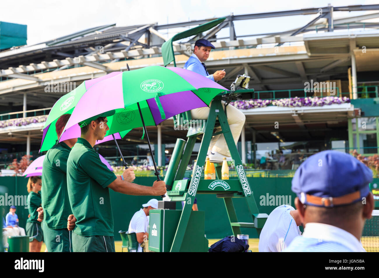 Wimbledon court attendants hold up umbrellas to shade players from the