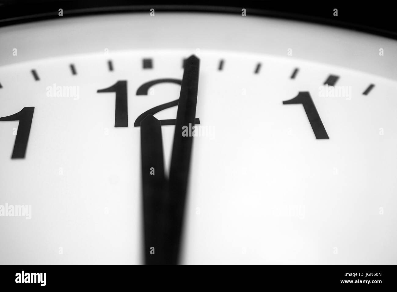 Closeup and selective on the pointers of a clock marking a minute after midnight - black and white rendering. The main focus is on the number twelve a Stock Photo