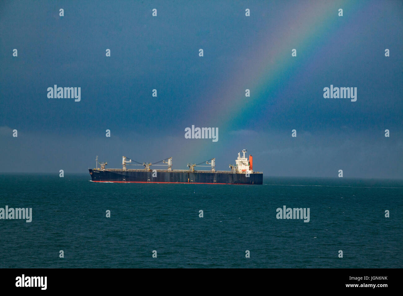 Freighter sailing across the ocean with a rainbow Touching the ship. Stock Photo