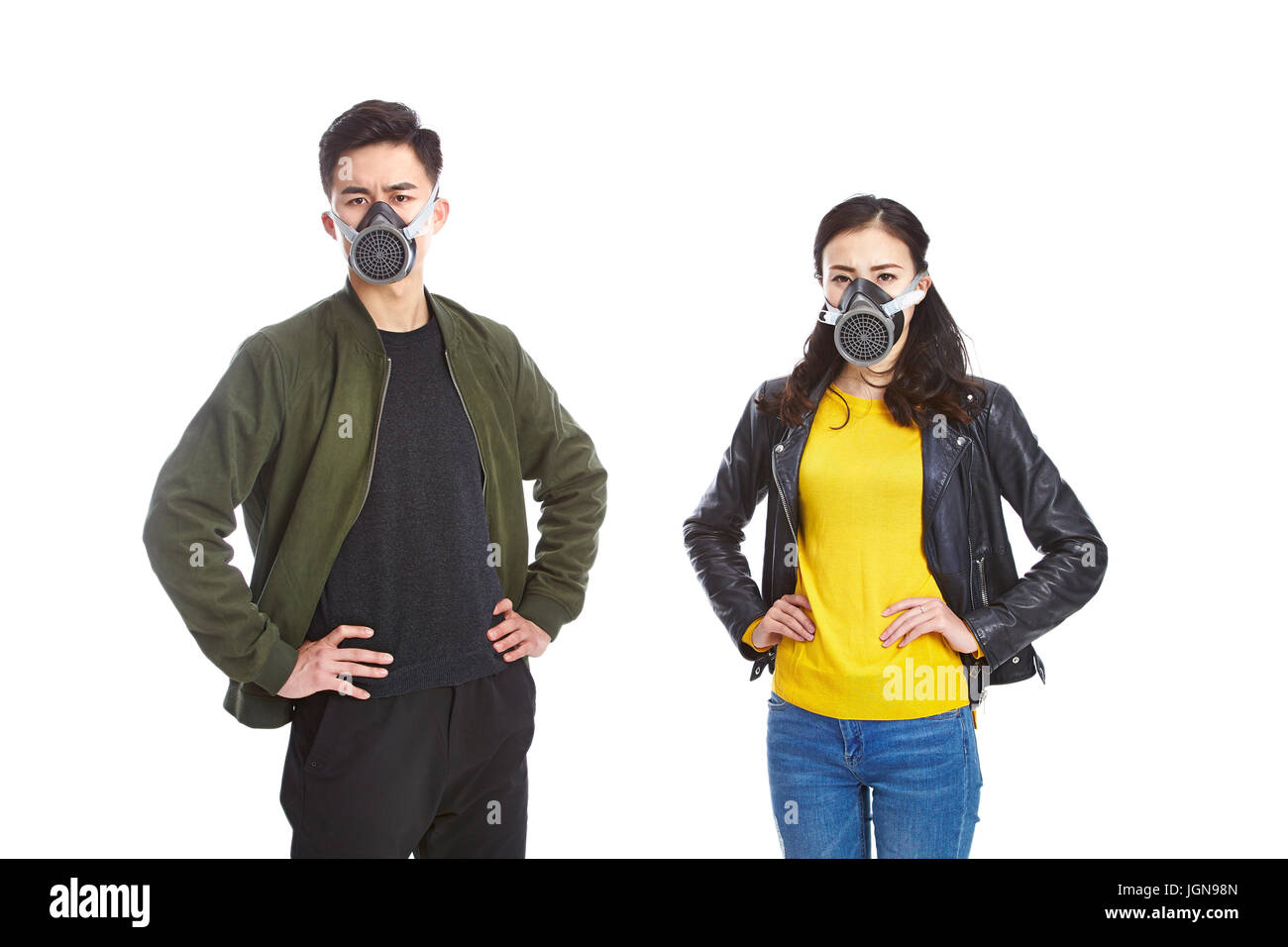 young asian man and woman wearing gas mask staring at camera with arms akimbo, isolated on white background. Stock Photo