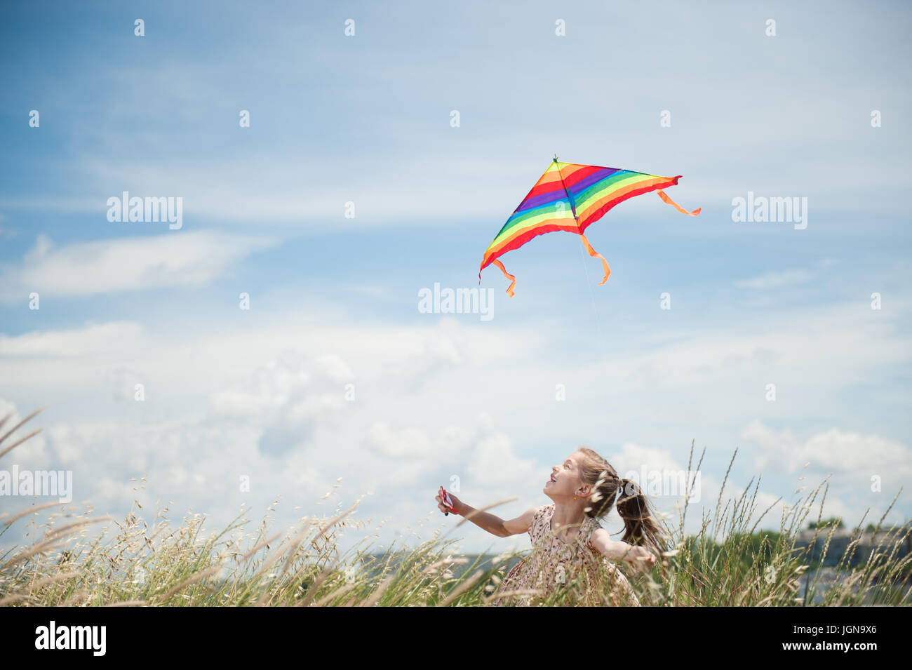 happy smiling little girl holding flying kite in field on blue cloudy ...