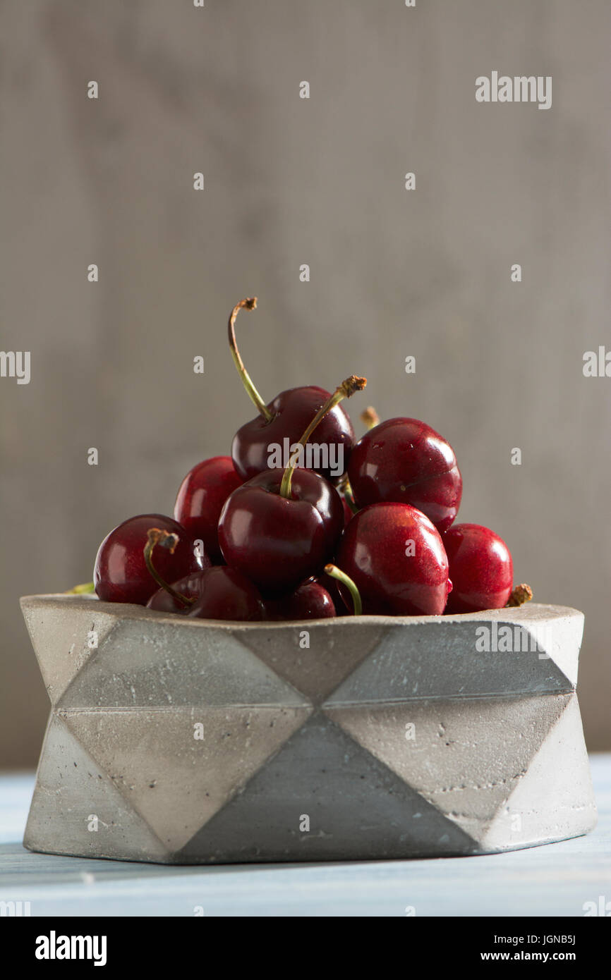 delicious cherries in geometrico concrete bowl on rustic texture, Stock Photo