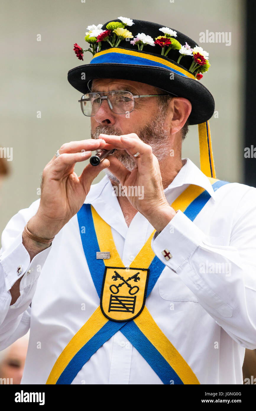 Traditional folk dancer, Yateley Morris man playing the flute, recorder. Male, 40s, wearing hat with flowers on, Morris costume. Outdoors. Stock Photo