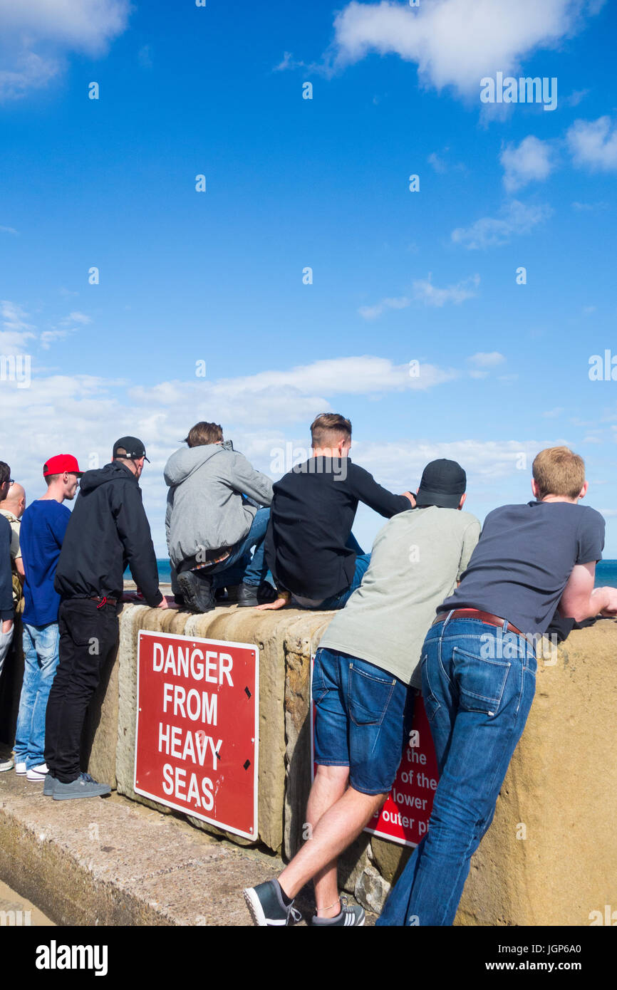 Teenagers wave watching from sea wall. UK Stock Photo