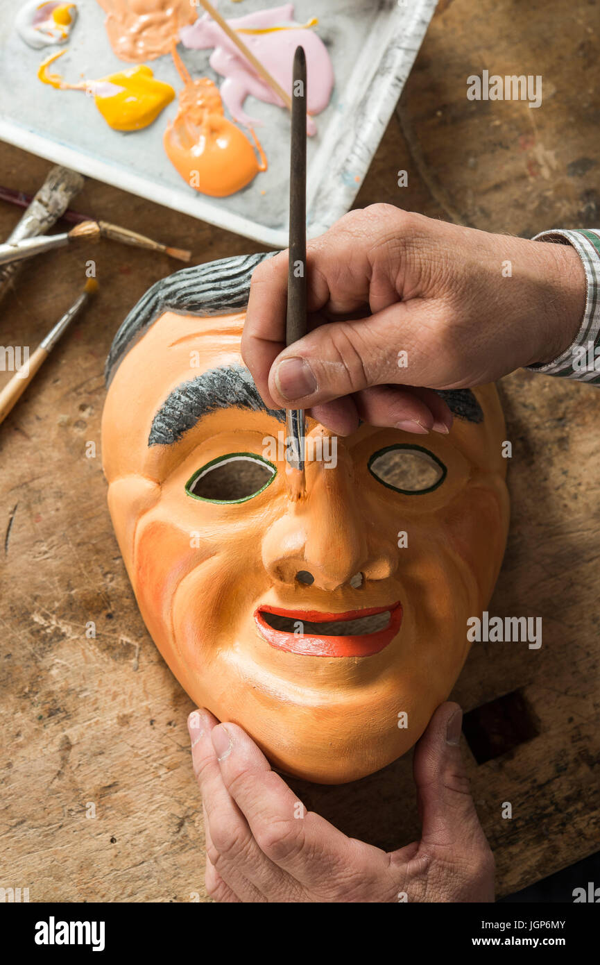 Painting the face of a wooden mask with a paintbrush, on a workbench, wooden mask carver, Bad Aussee, Styria, Austria Stock Photo