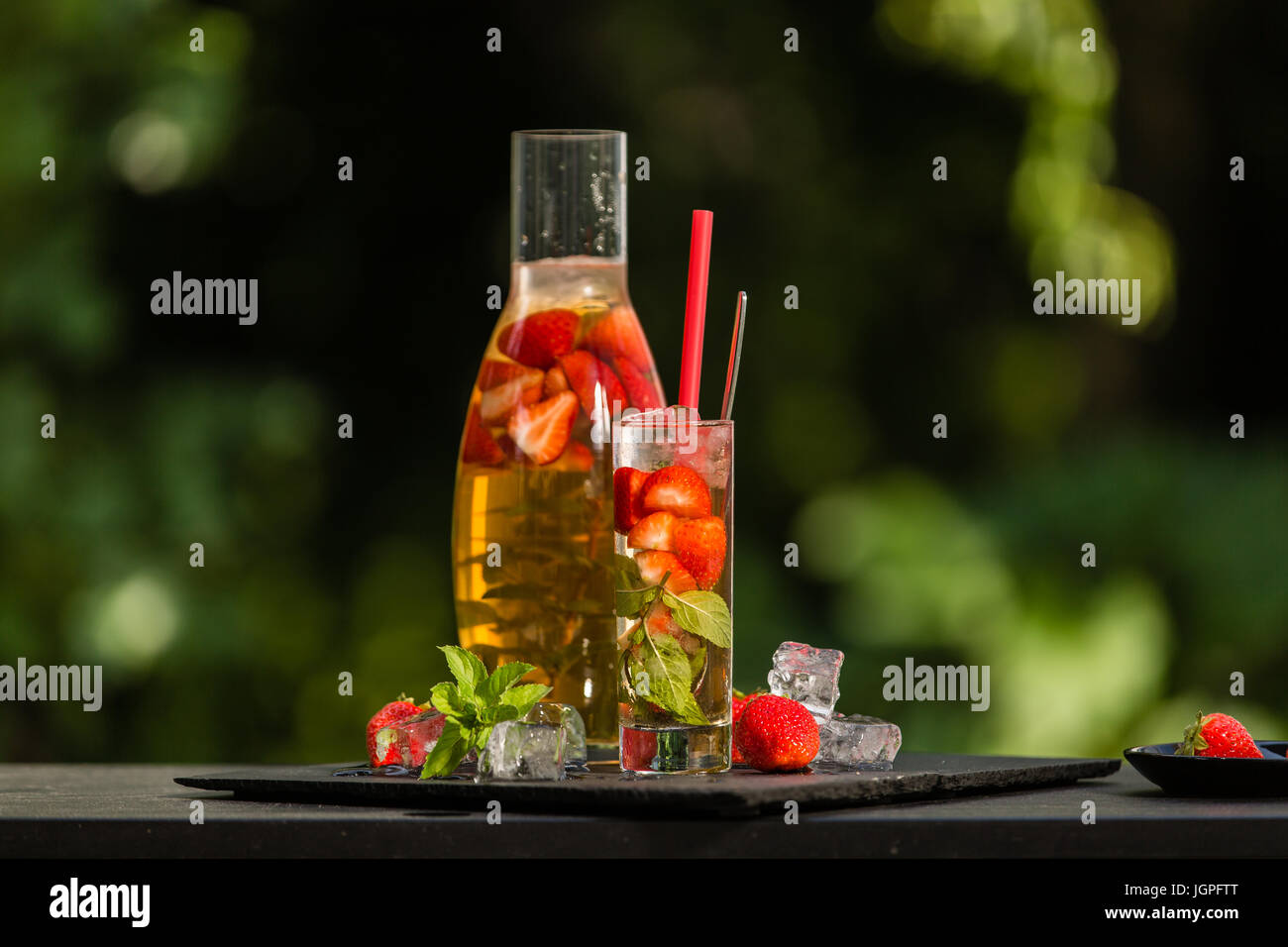 Homemade strawberry ice tea in the garden. Strawberries, mint and lemon balm leaves, ice and green tea. Stock Photo