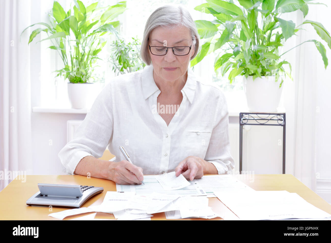 Senior german woman at home with a calculator and lots of bills and receipts, filling out the printed forms of the annual tax declaration Stock Photo