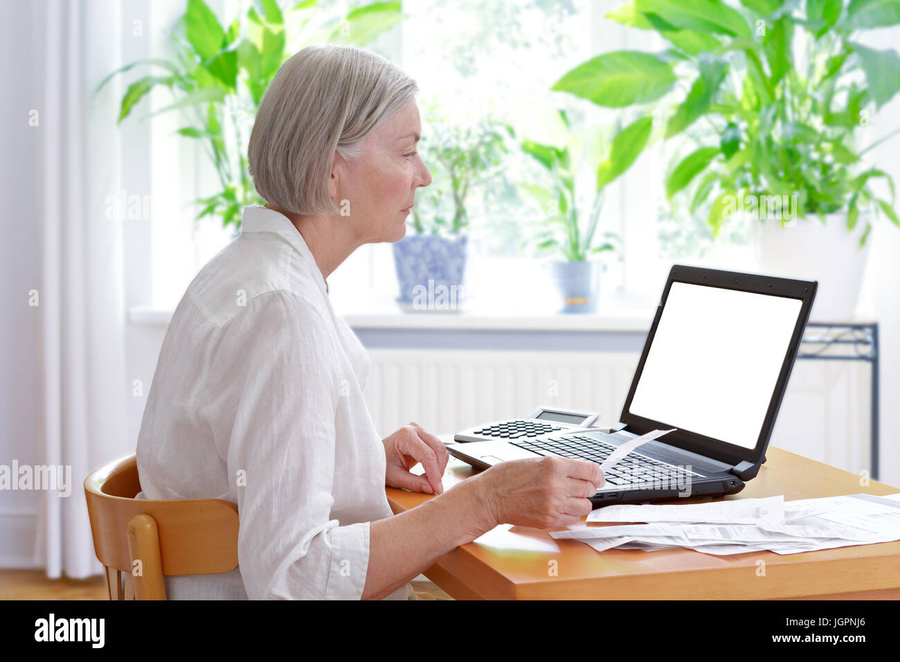 Senior woman at home with a calculator and lots of receipts in front of her laptop making her annual tax declaration, white screen, copy space, templa Stock Photo