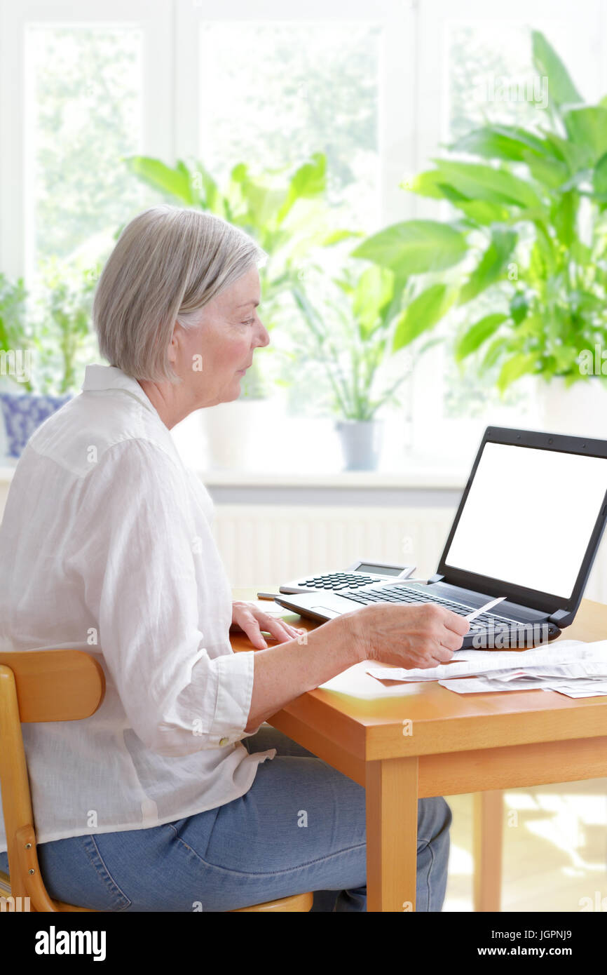 Senior woman at home with a calculator and lots of receipts in front of her laptop making her annual tax declaration, blank screen, copy space, templa Stock Photo