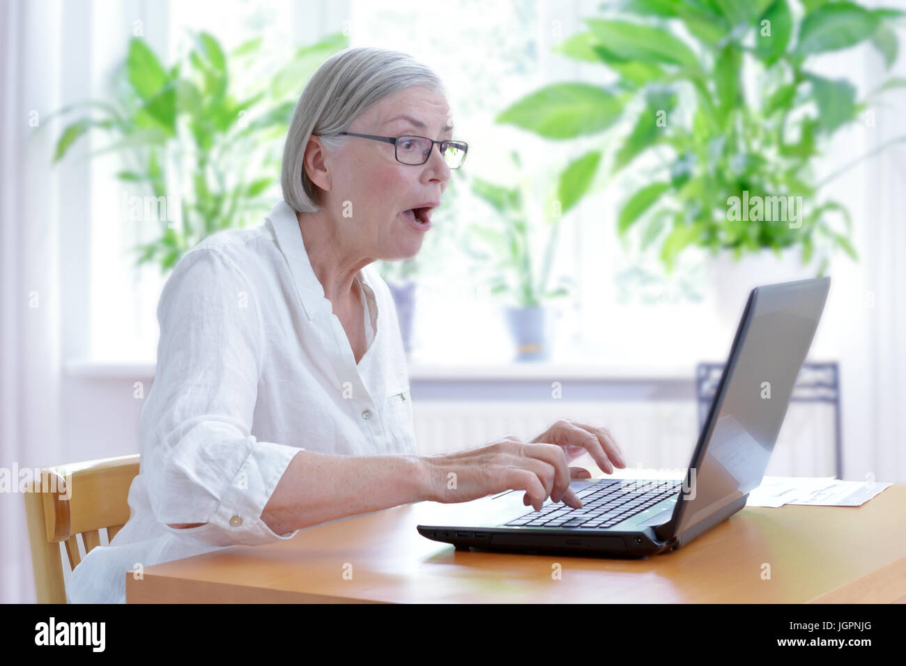 Senior woman at home in her living room staring in extreme shock at the screen  of her laptop, internet security concept Stock Photo