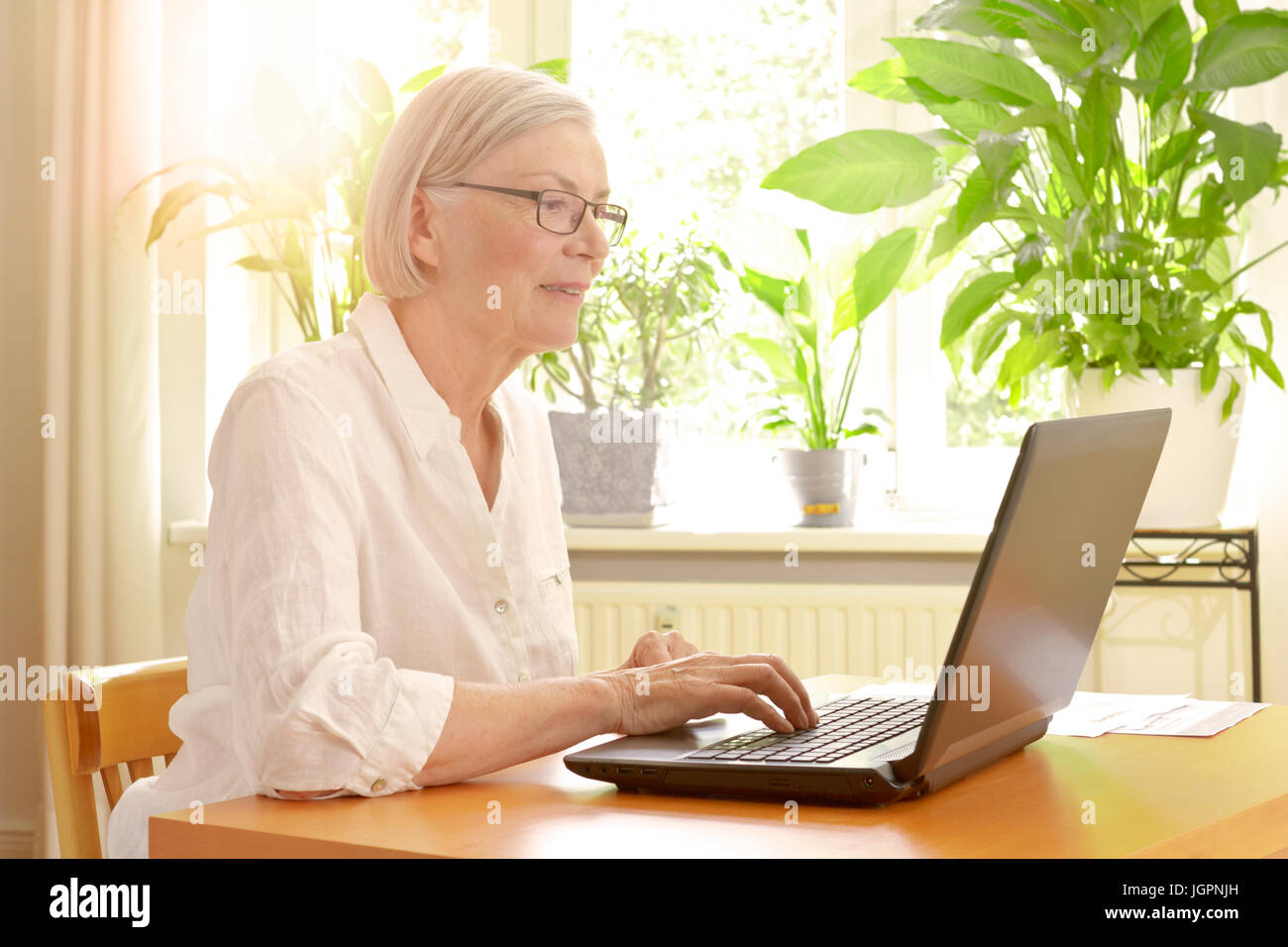 Happy senior woman in her sunny living room in front of her laptop enjoying the benefits of good financial planning for a carefree retirement Stock Photo
