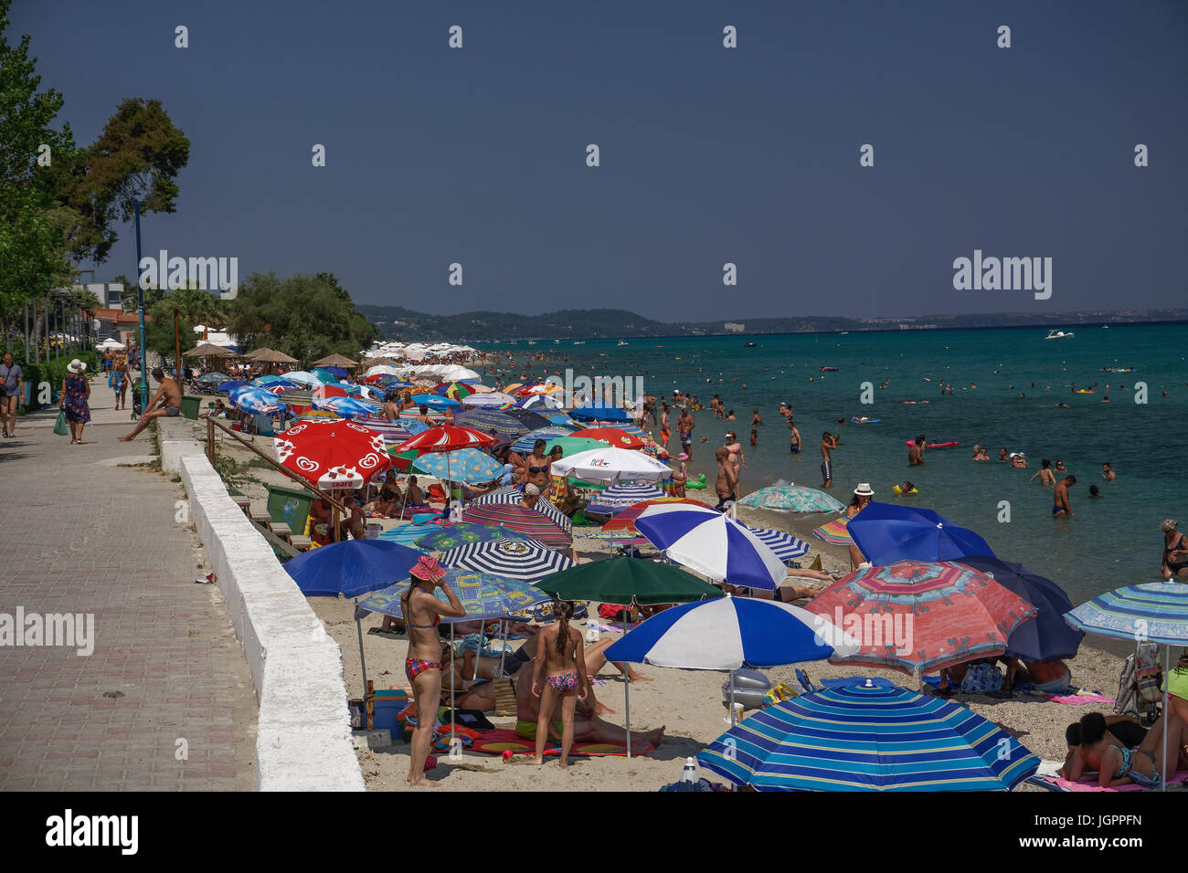 Bathers on the beach on a hot summer day at Greece. Sunbathers on a beach with beach umbrellas at Chaniotis, Chalkidiki peninsula. Stock Photo