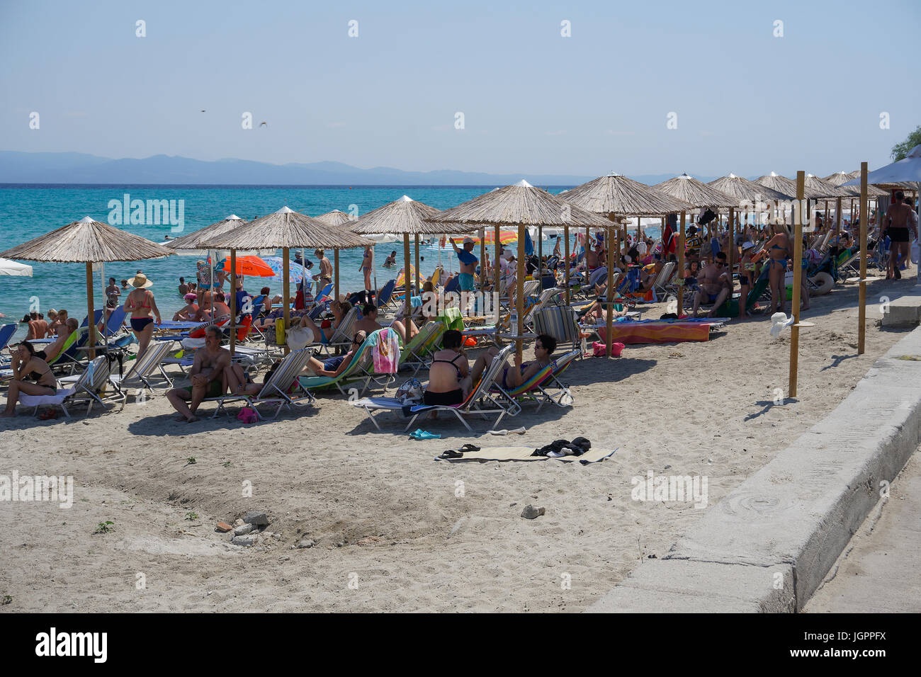 Bathers on the beach on a hot summer day at Greece. Sunbathers on a beach with beach umbrellas at Chaniotis, Chalkidiki peninsula. Stock Photo