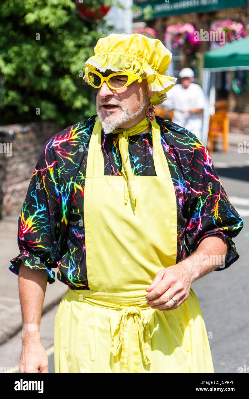 Seven Champions morris dancer, traditional morris 'fool', man, 40s, wearing  yellow apron and yellow shower hat with yellow framed glasses. Standing in  street, front view, head turned to look away Stock Photo -