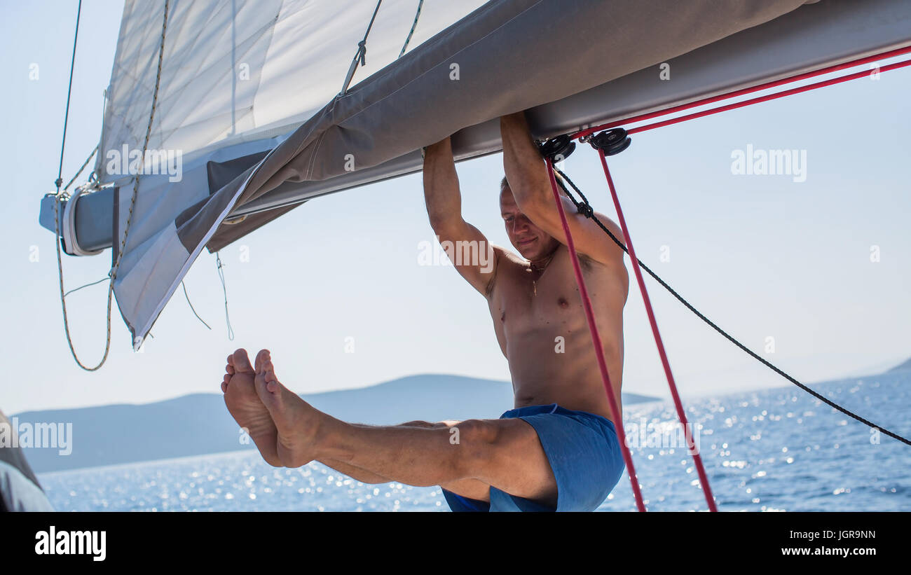 Young man pulled on the hand on the mast of a sailing yacht. Stock Photo