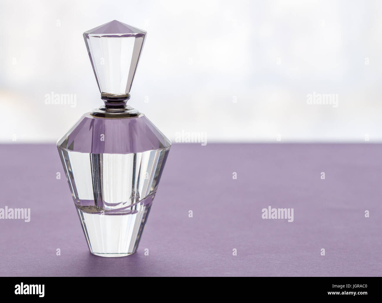 Empty vintage crystal glass perfume bottle with stopper on lilac background Stock Photo