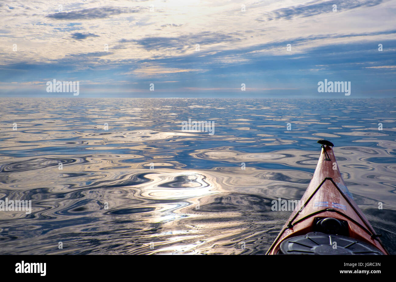 A sea kayak heading out into a calm, empty sea, Anglesey, Wales , UK Stock Photo