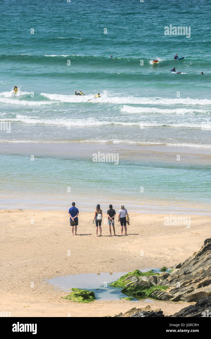 Holidaymakers standing on Fistral beach watching surfers in the sea. Stock Photo