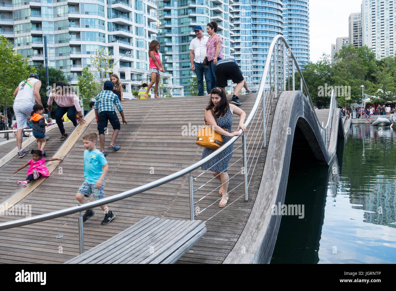 Tourists and pedestrians attempt to walk on the Simcoe Wave Deck an imaginative example of urban art at Harbourfront in downtown Toronto Ontario. Stock Photo
