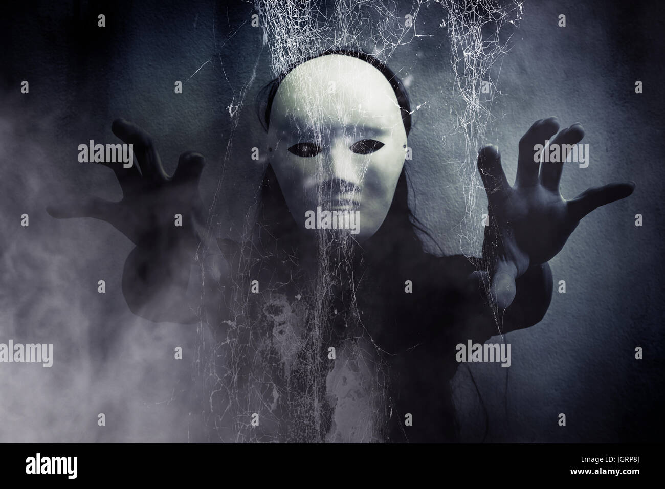 Mysterious woman in black wearing white mask hidden behind spider web,Scary background for book cover Stock Photo