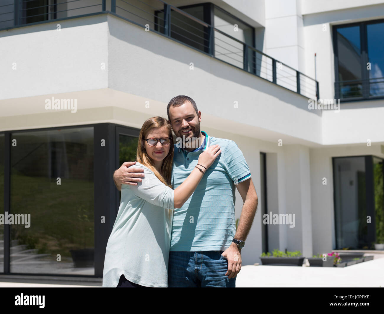 Portrait of a happy young couple hugging in front of their new luxury ...