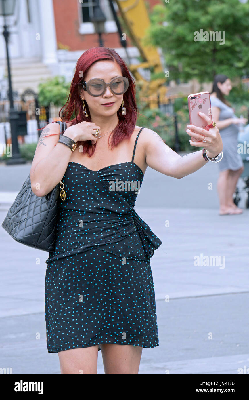 An attractive Asian woman with bright red hair and a tattoo takes a selfie in Washington Square Park in Greenwich Village in New York City Stock Photo