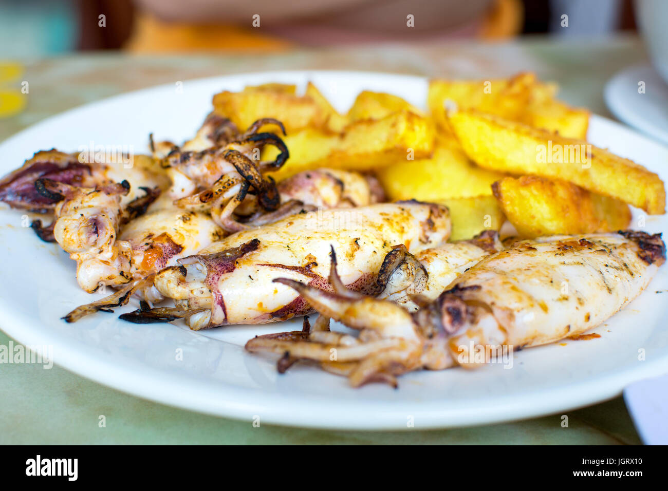 Grilled squid with french fries on a plate. Seafood meal Stock Photo