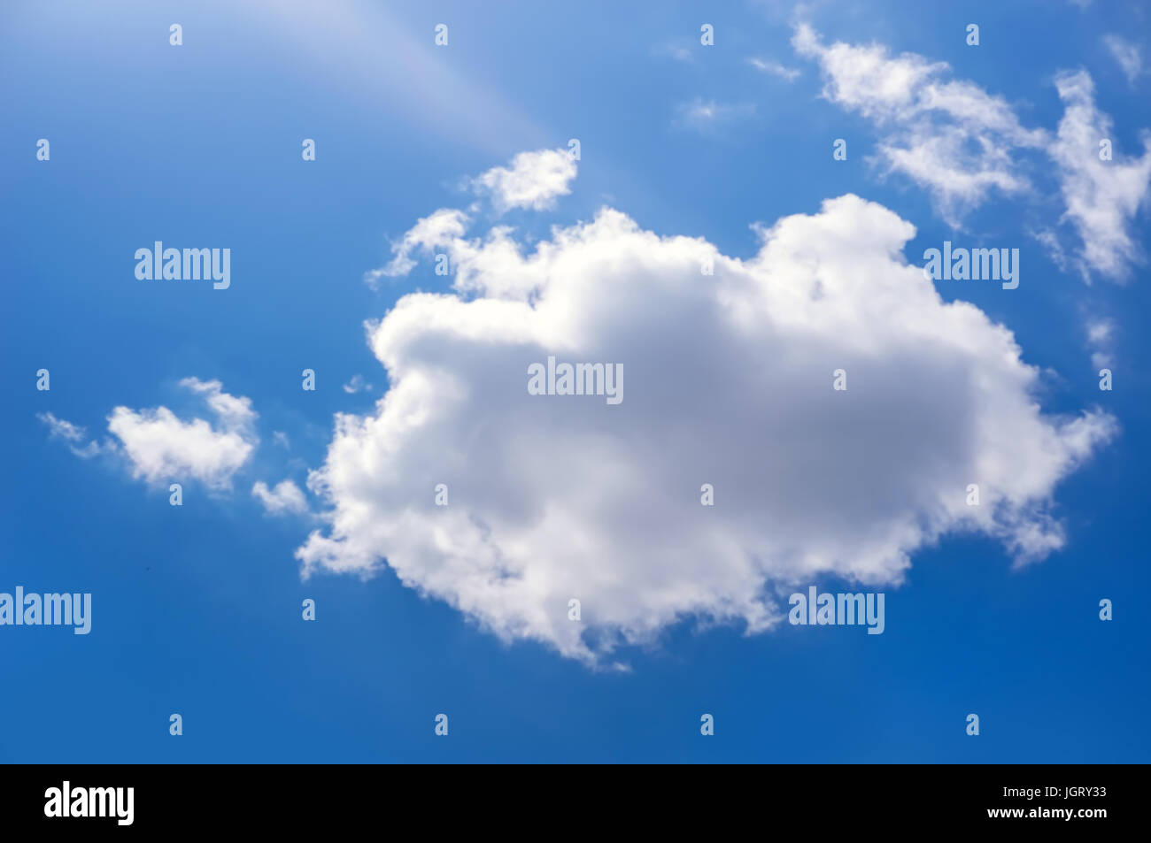 The sun is bright shining blue through a small cloud. Cumulus clouds in the blue sky. The sun shines through white cloud. Stock Photo
