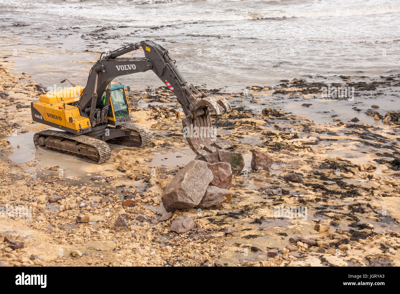 A workman using a JCB on the beach at Hartlepool,England,UK, to build up the sea defenses Stock Photo