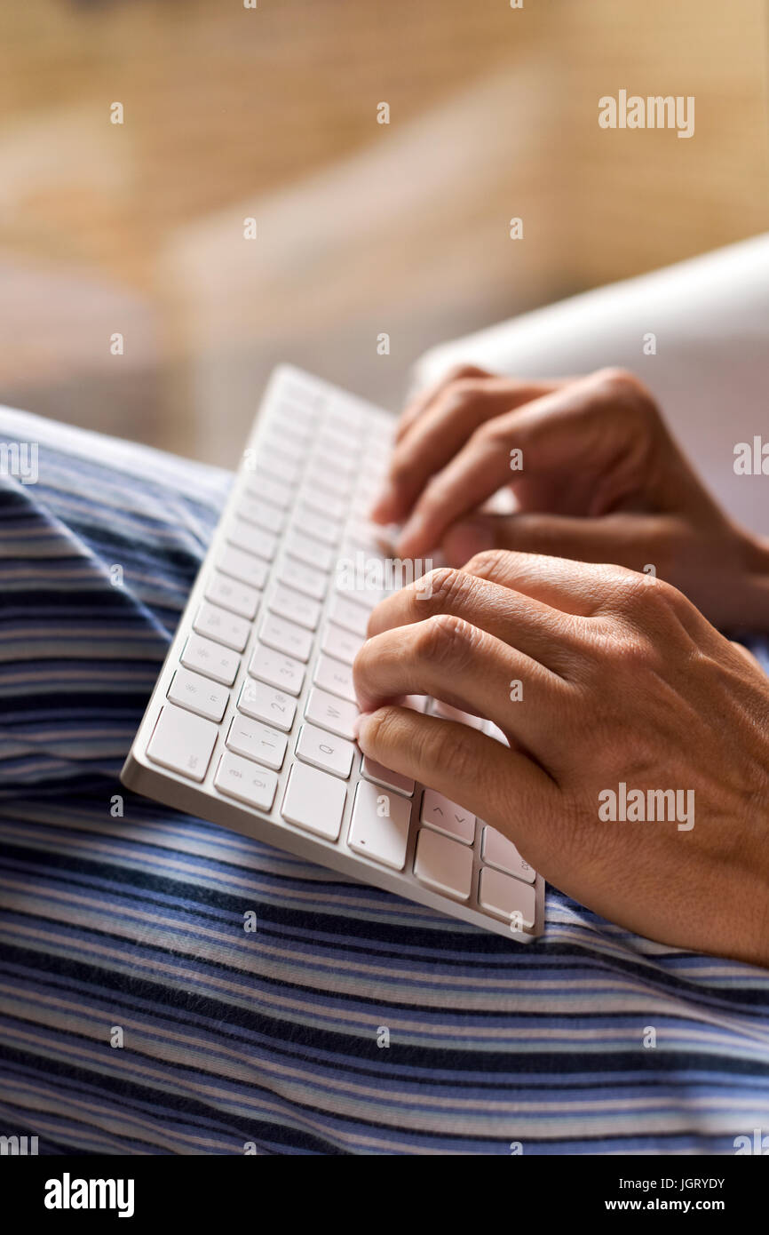 closeup of a young caucasian man in pajamas sitting in a comfortable armchair typing in a computer keyboard Stock Photo