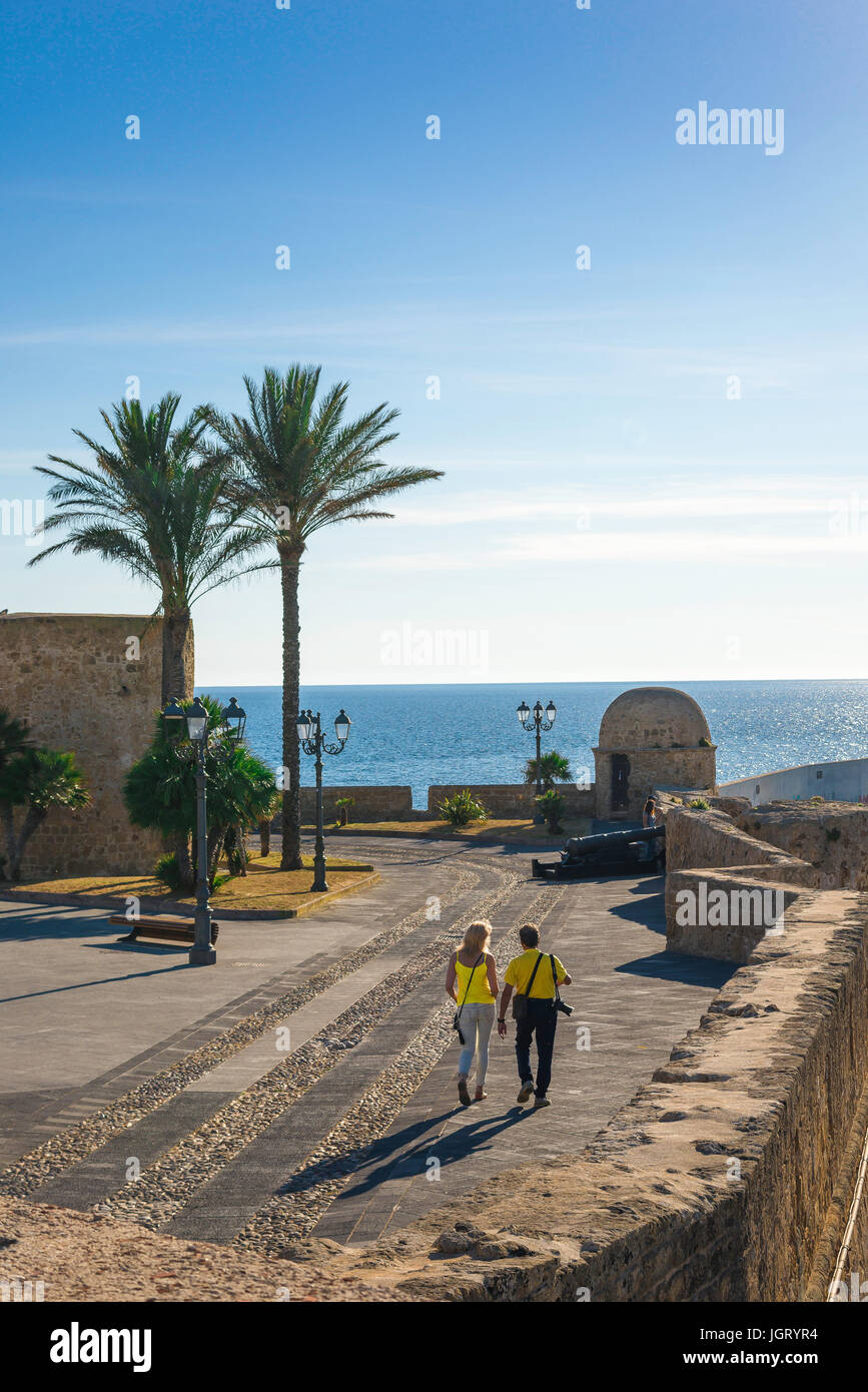 Couple Mediterranean holiday, a man and a woman stroll along the medieval seawall in the harbour area of Alghero, Sardinia, Italy. Stock Photo