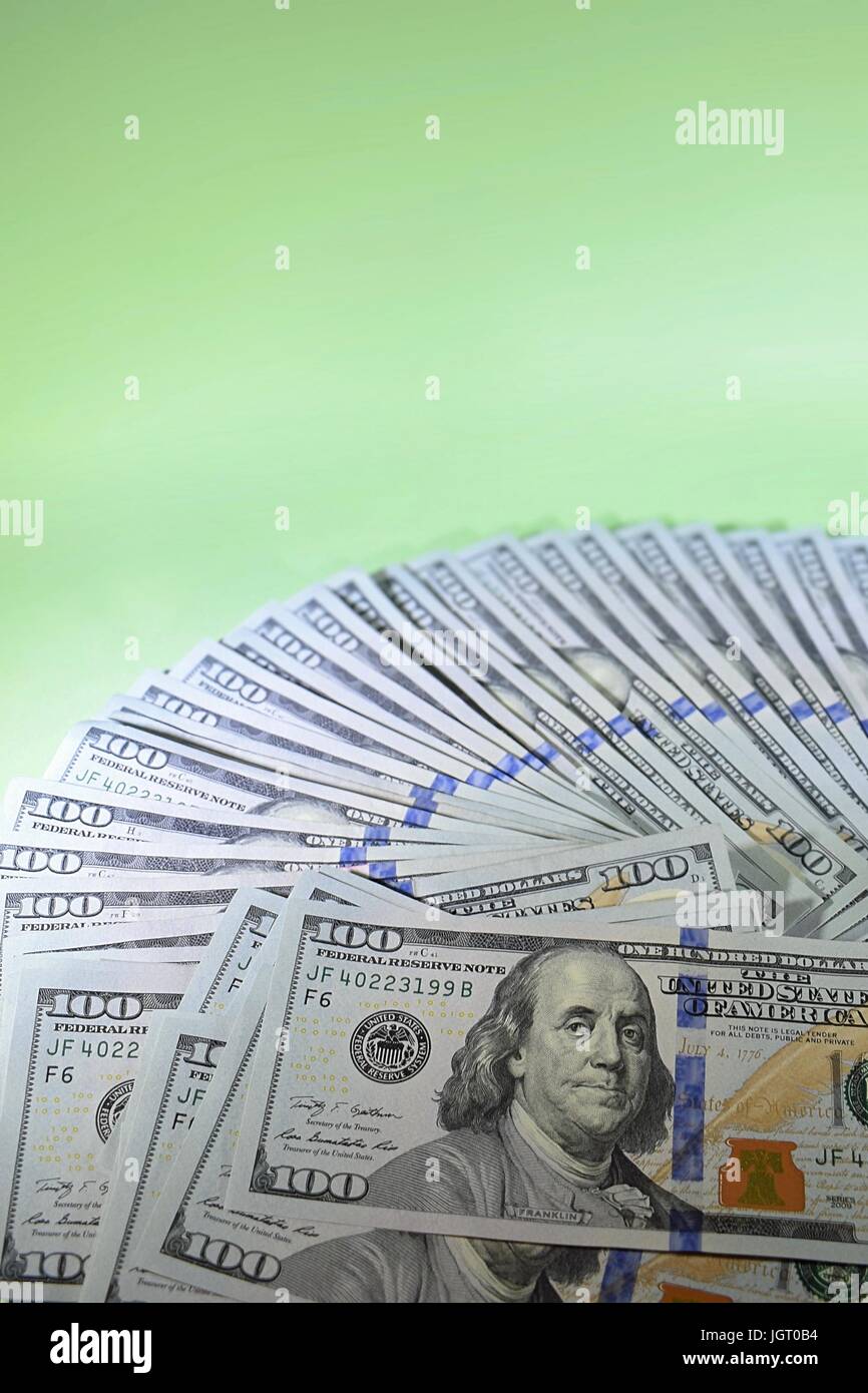 new hundred dollar bills American $100 USD cash money fanned out in a circle filling half the frame with messy pile on a green background Stock Photo