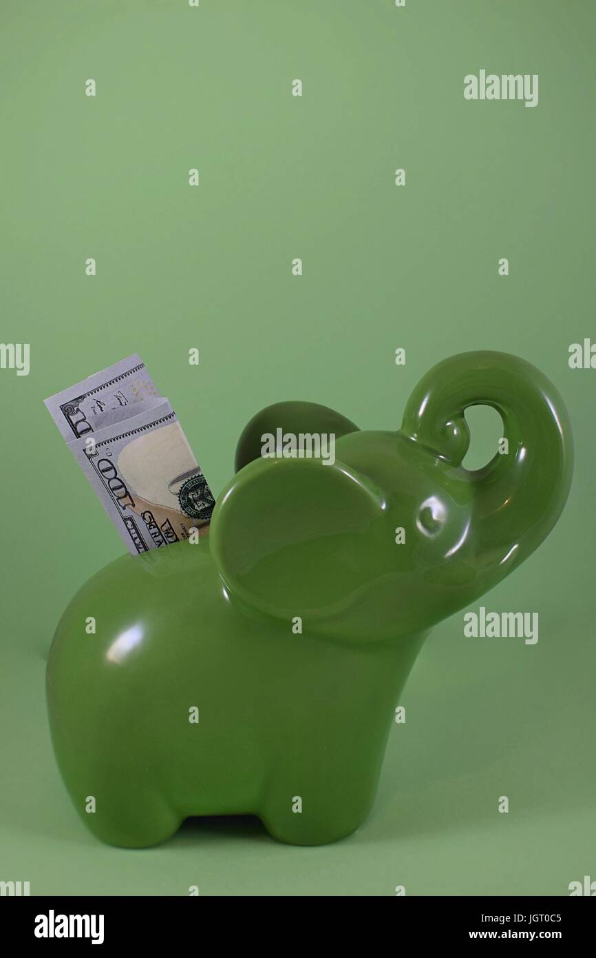 green elephant piggy bank with new one hundred dollar bill $100 USD savings being inserted on green background Stock Photo