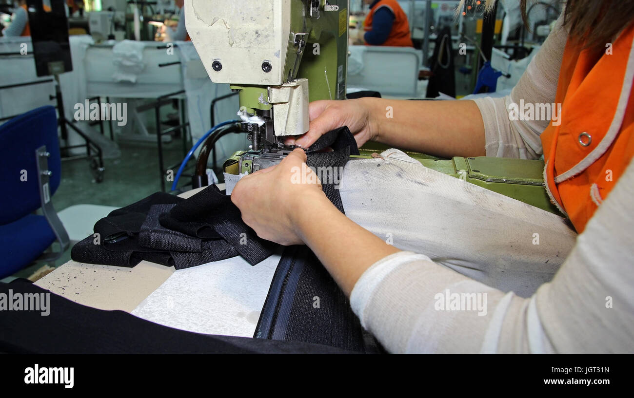 Employees work at a production line of a garment factory. Industrial sewing machine close up. Textile industry. Stock Photo