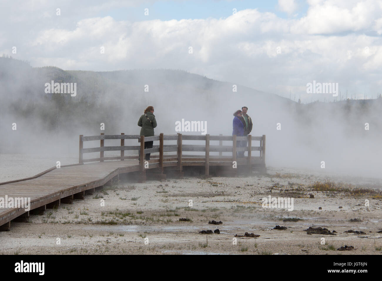 Three people are standing on the boardwalk in the steam produced by Rainbow Pool in Black Sand Basin, Upper Geyser Basin, Yellowstone National Park Stock Photo