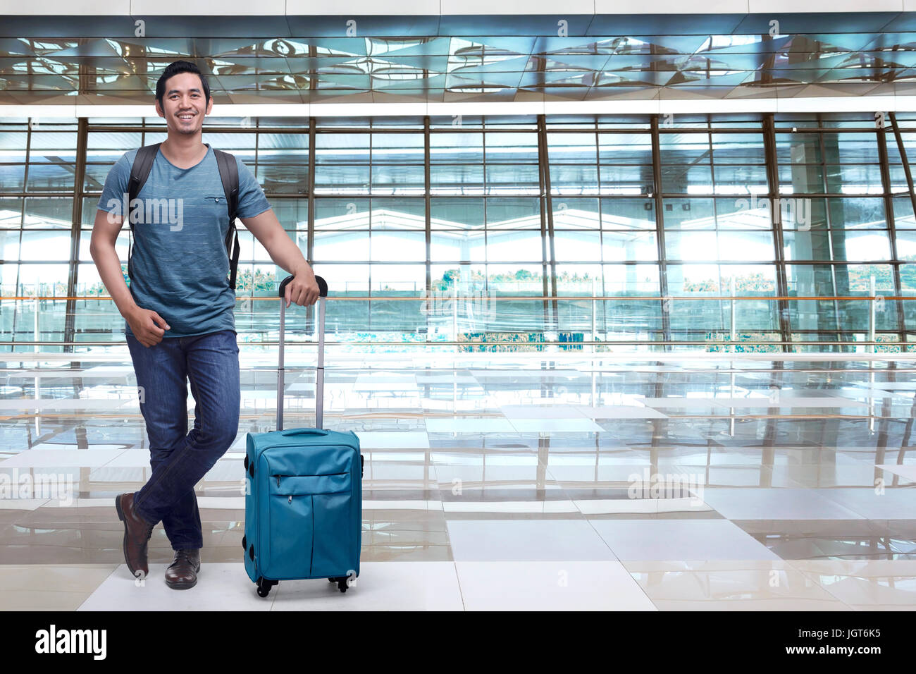 Handsome asian man backpacker holding blue suitcase in the airport terminal Stock Photo