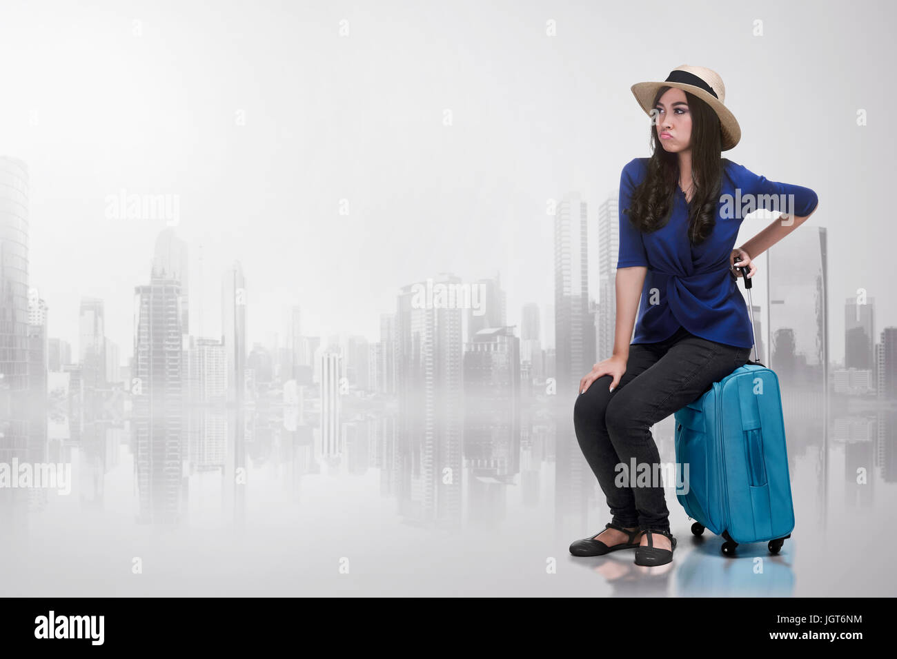 Young asian woman with unhappy face sitting on a suitcase over abstract background Stock Photo