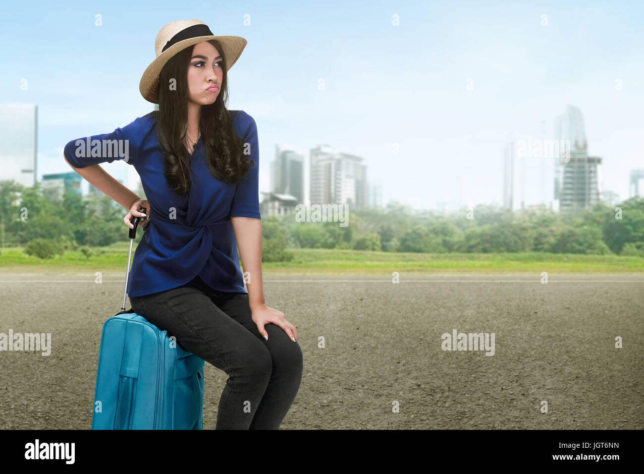 Traveler asian woman with hat sitting on a suitcase on the urban road Stock Photo