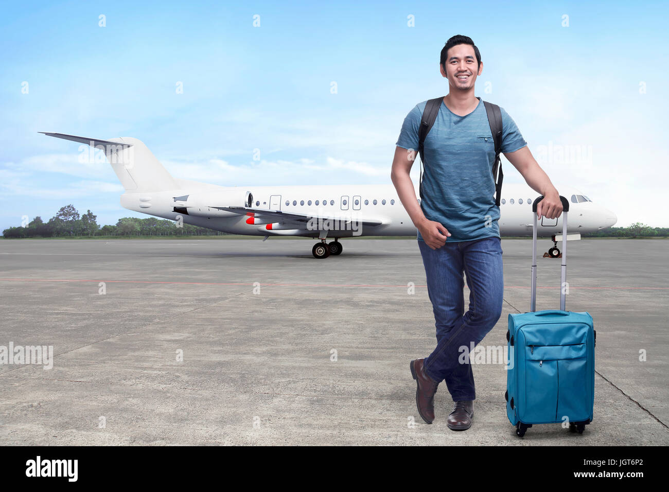 Handsome asian backpacker with suitcase standing against plane background Stock Photo