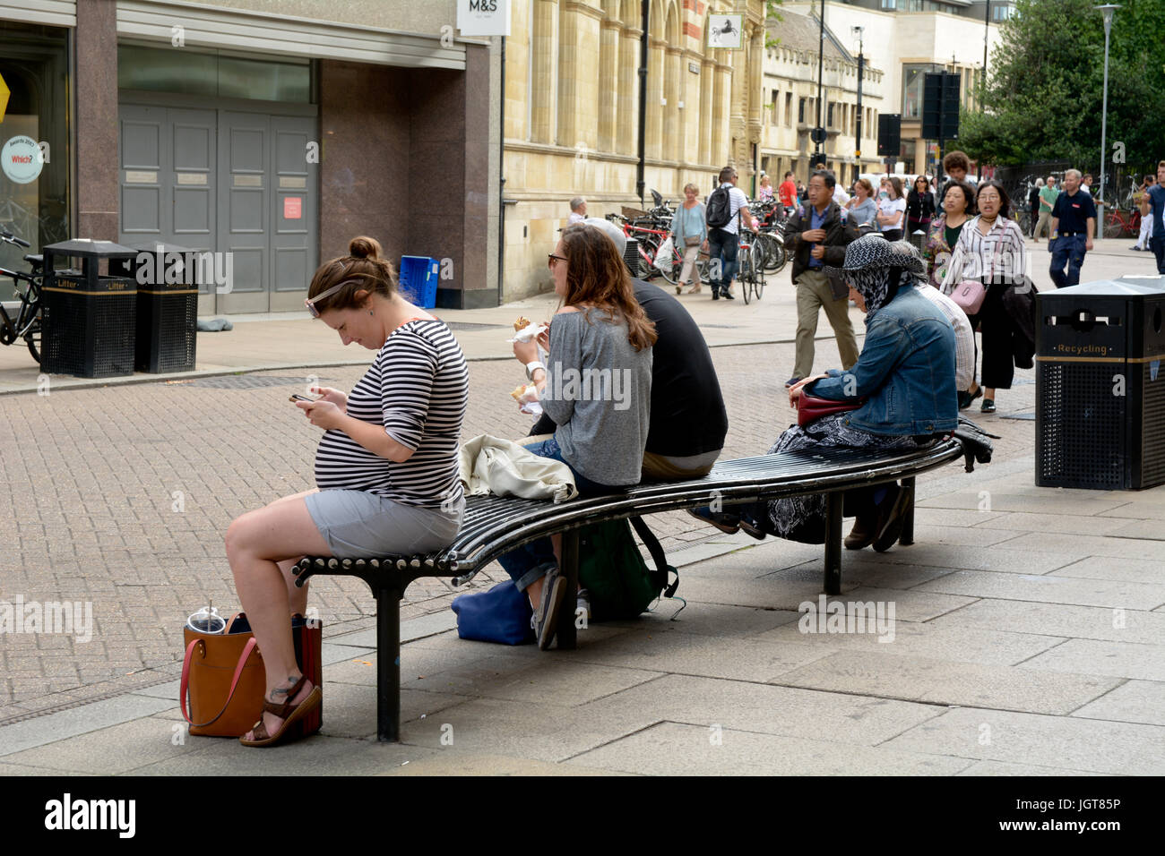 People sitting down on bench in the centre of Cambridge on hot summers day in Cambridgeshire England Stock Photo