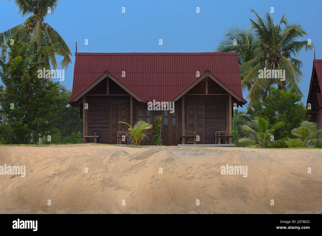 Wooden beach front holiday resort chalet onto of golden sand dune with palm tree and blue sky. Stock Photo