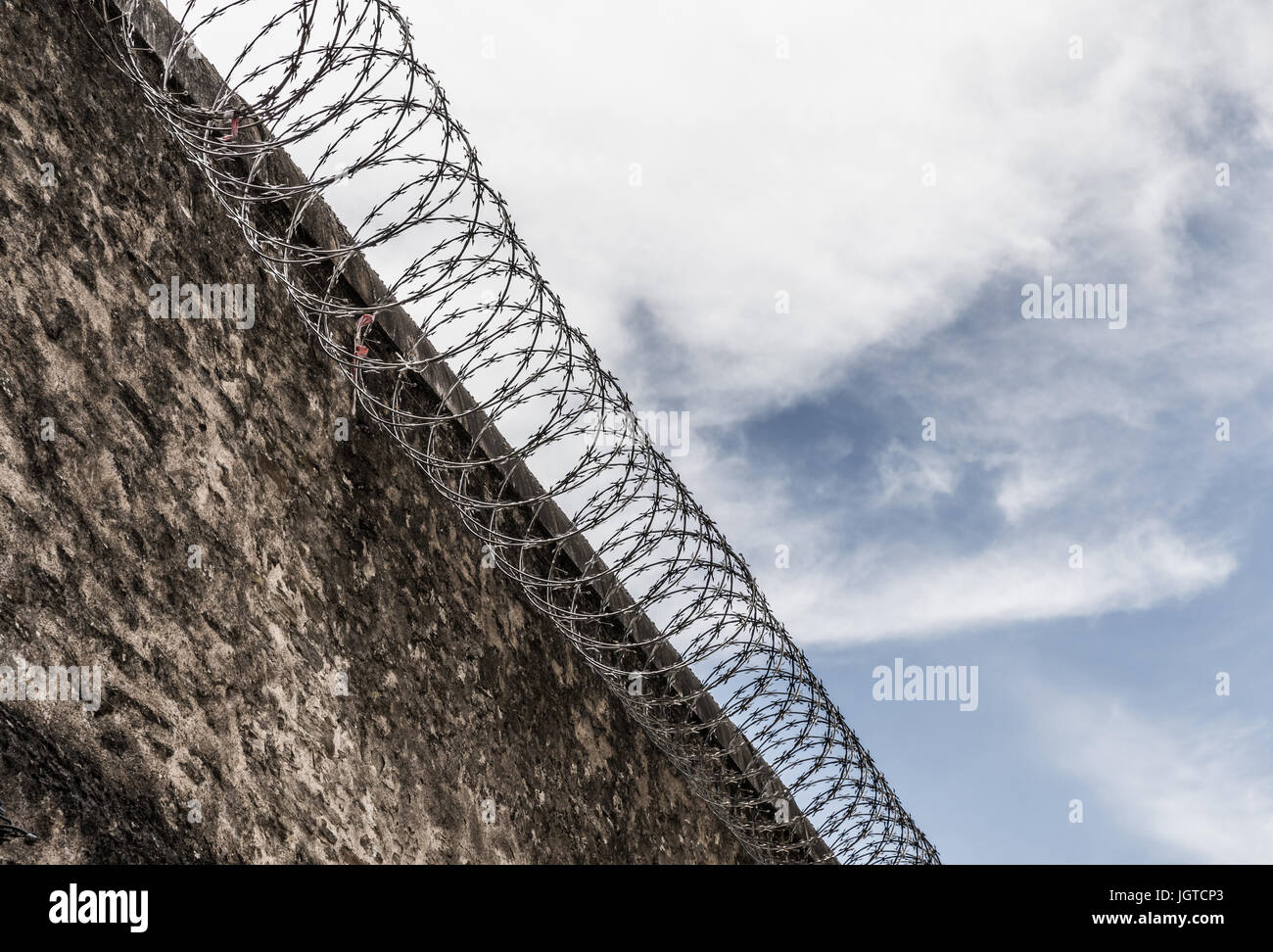 Concrete wall of the prison with cutting steel barbed wire Stock Photo