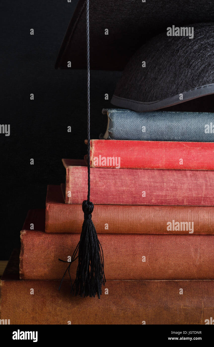 A pile of old, used vintage books, arranged as steps leading up to a graduation cap at the top (mortarboard). Stock Photo
