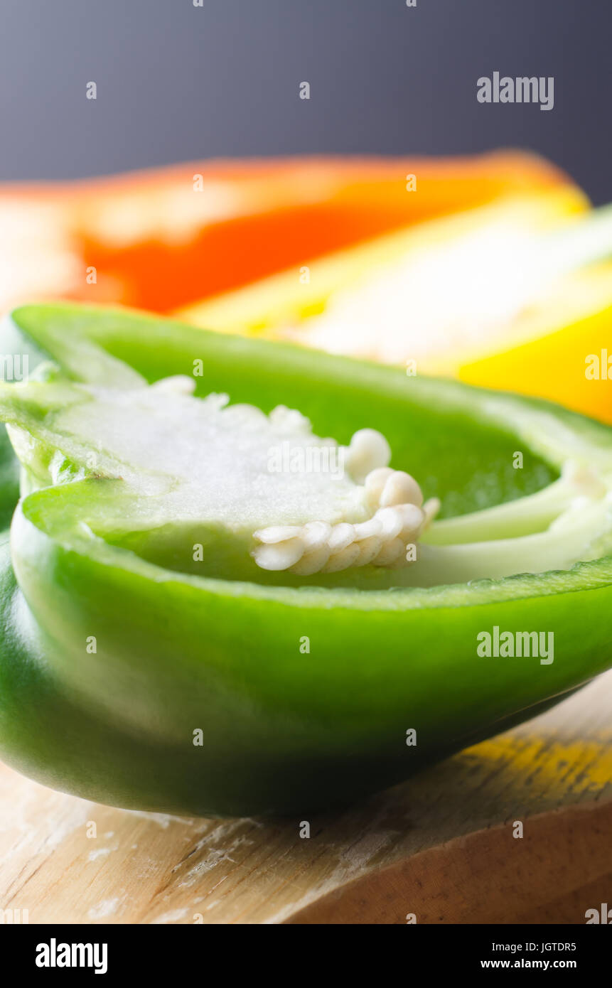 Close up (macro) shot of three bell peppers, cut in half on a wooden chopping board with seeds exposed.    Green pepper in foreground with yellow and  Stock Photo