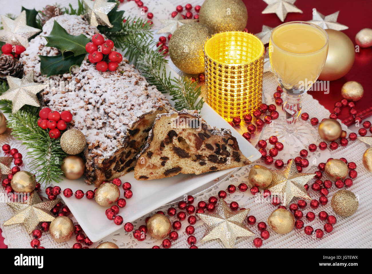Christmas chocolate stollen cake on a plate with egg nog, holly, fir and ivy and gold bauble and red bead decorations. Stock Photo
