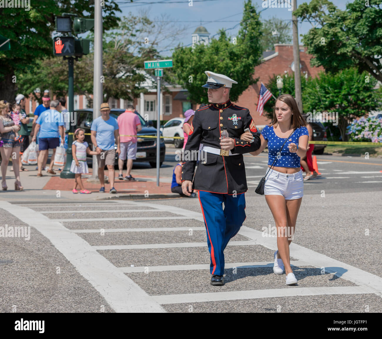 man in military uniform with woman crossing the street in Southampton, ny during a fourth of july parade Stock Photo