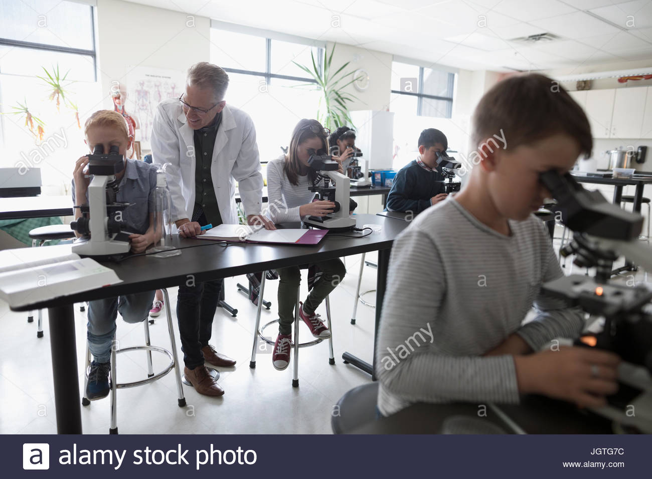 Teacher helping middle school students using microscopes, conducting