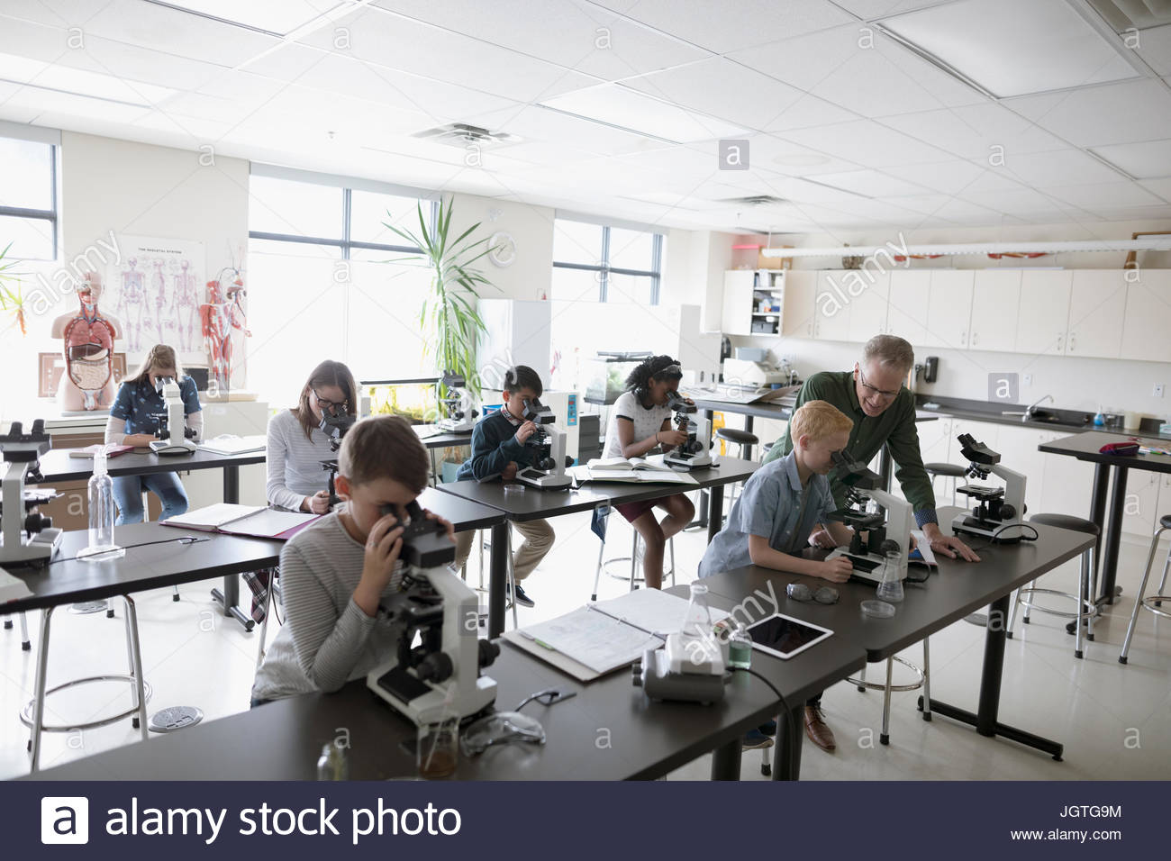 Teacher and middle school students using microscopes, conducting