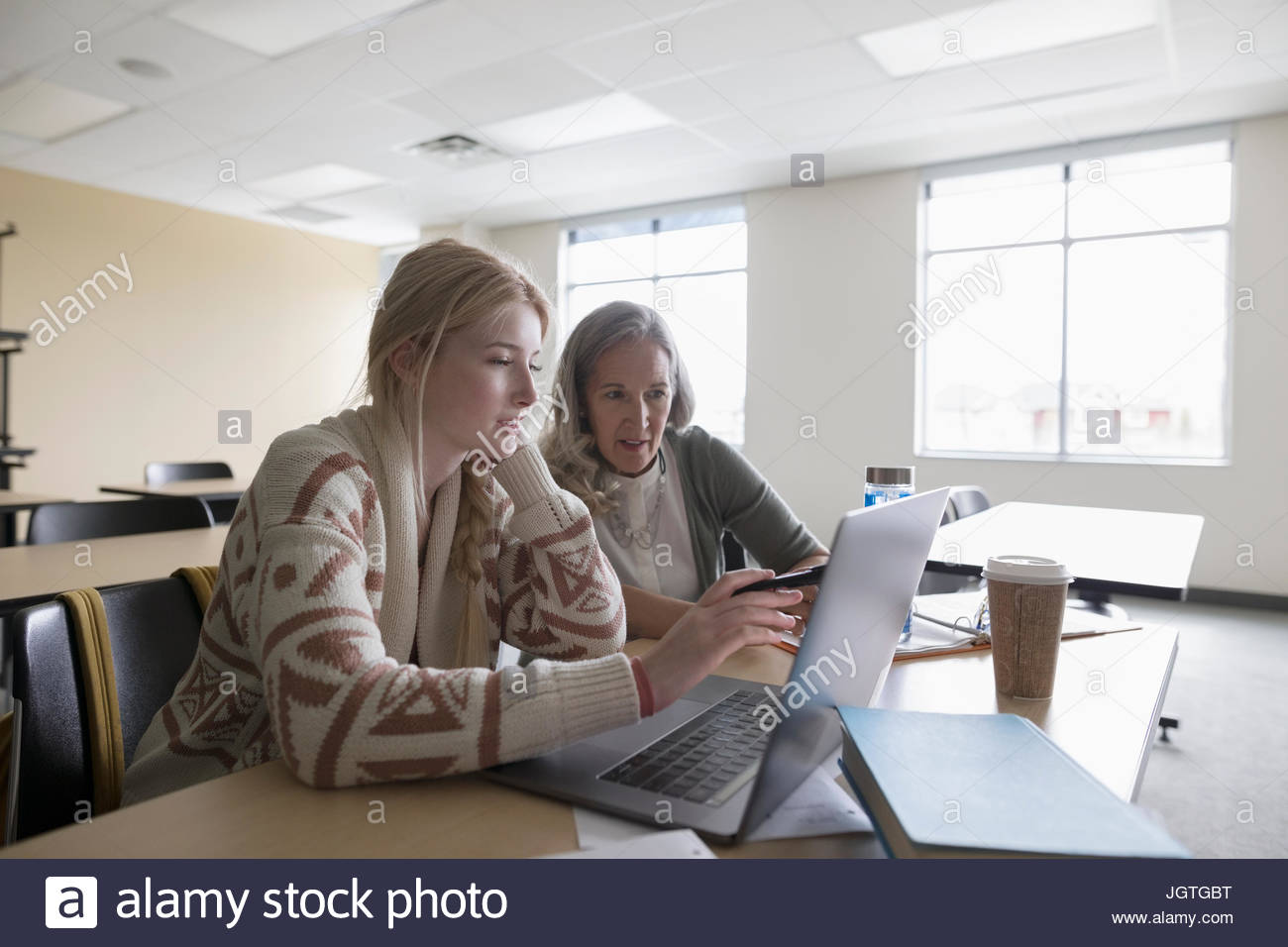 Female college professor helping student at laptop in classroom Stock