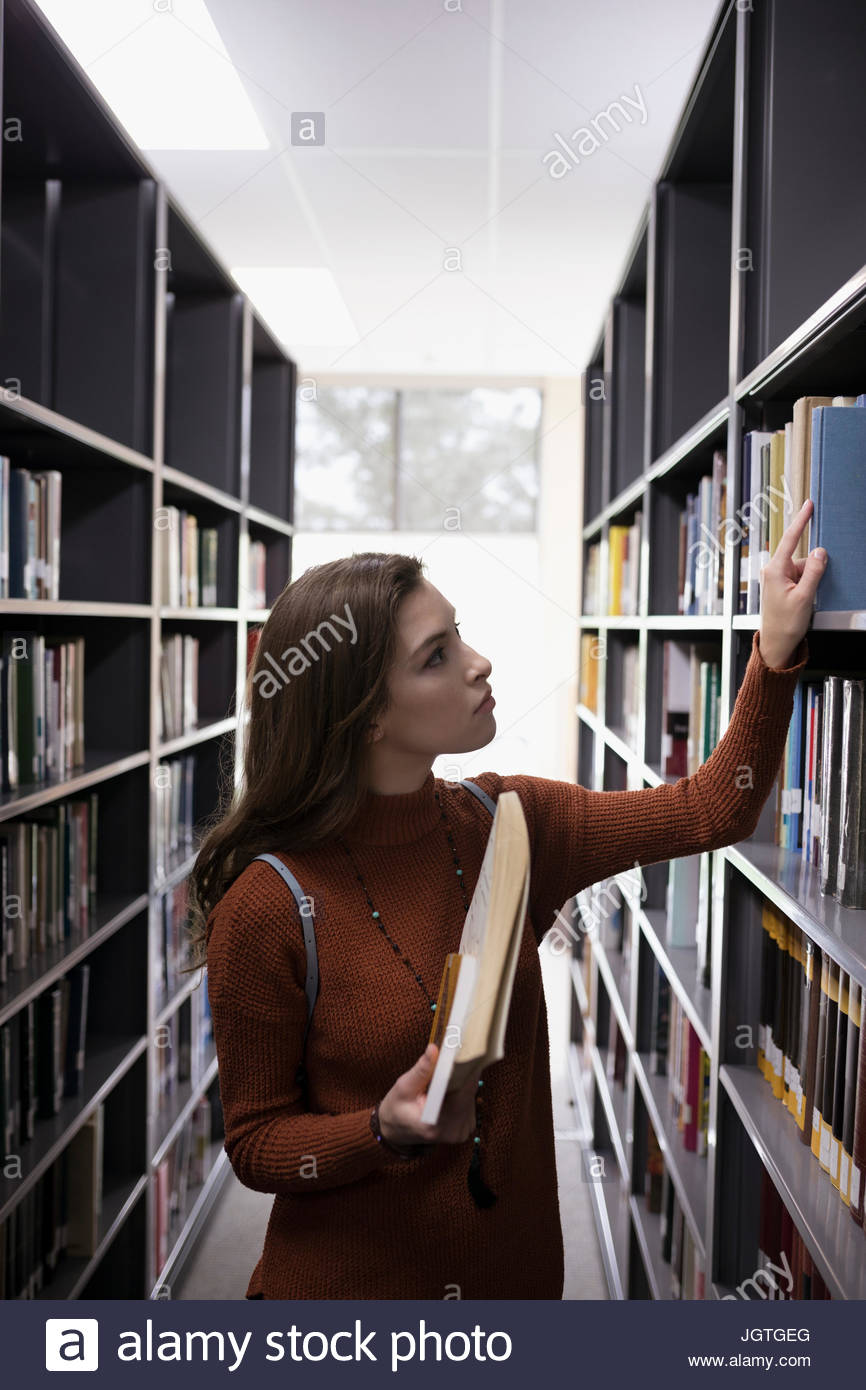 Female college student looking at books on bookshelves in library Stock Photo Alamy